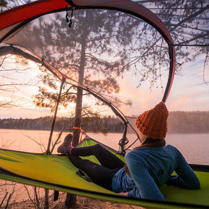 Women wearing Cloudline hiking socks laying in suspension tent by lake enjoying the sunset view.