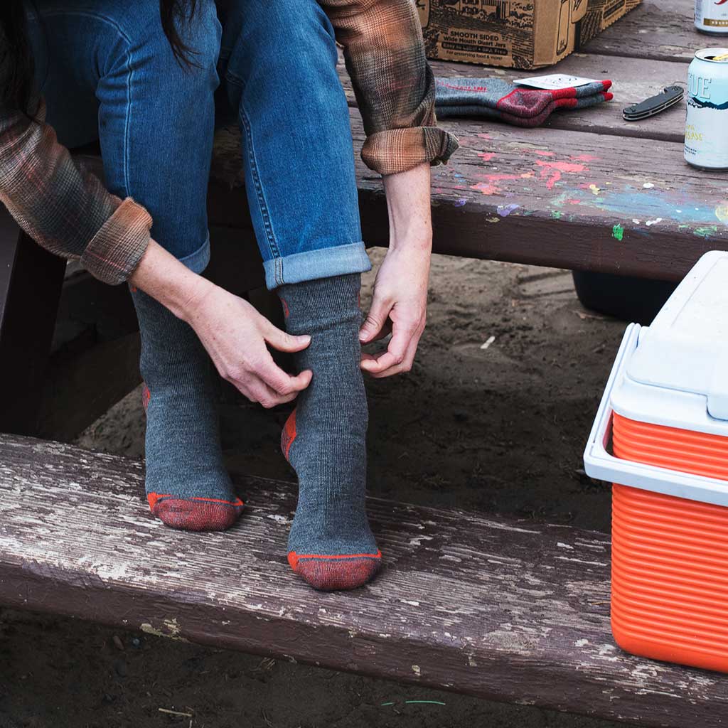 Women sitting on camp picnic table putting on Cloudline hiking socks. 