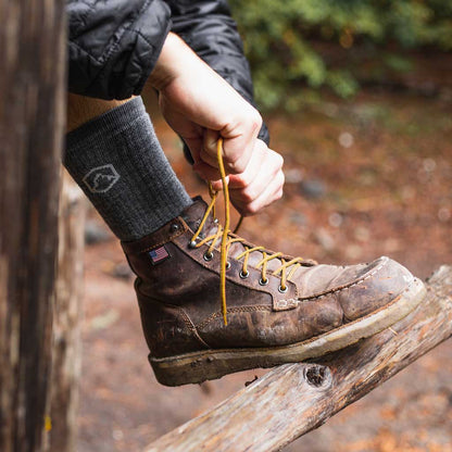 hiker wearing Cloudline hiking socks with foot up on log tying leather hiking boots. 