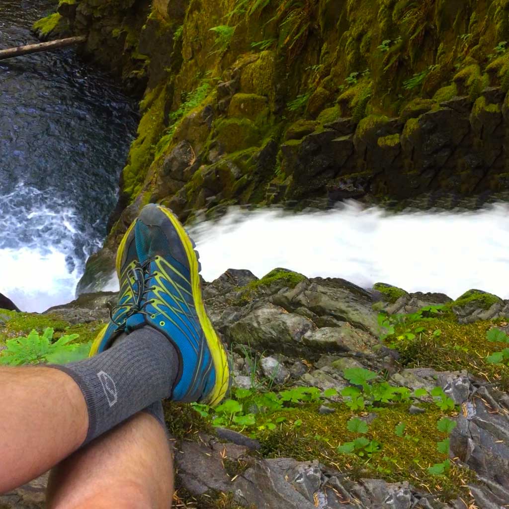 Hiker wearing Cloudline hiking socks, sitting above mossy waterfall.