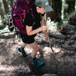 Backpacker wearing Cloudline hiking socks trekking up steep trail with walking stick.