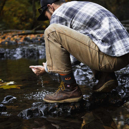 Man wearing Cloudline hiking socks crouching near water and scooping up water with hands. 