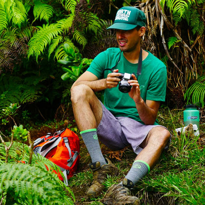 Photographer wearing Cloudline hiking socks sitting next to trail. 