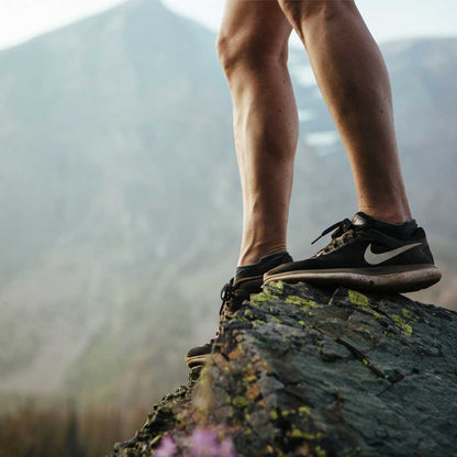 Trail runner wearing Cloudline running socks standing on big rock with mountain in background. 