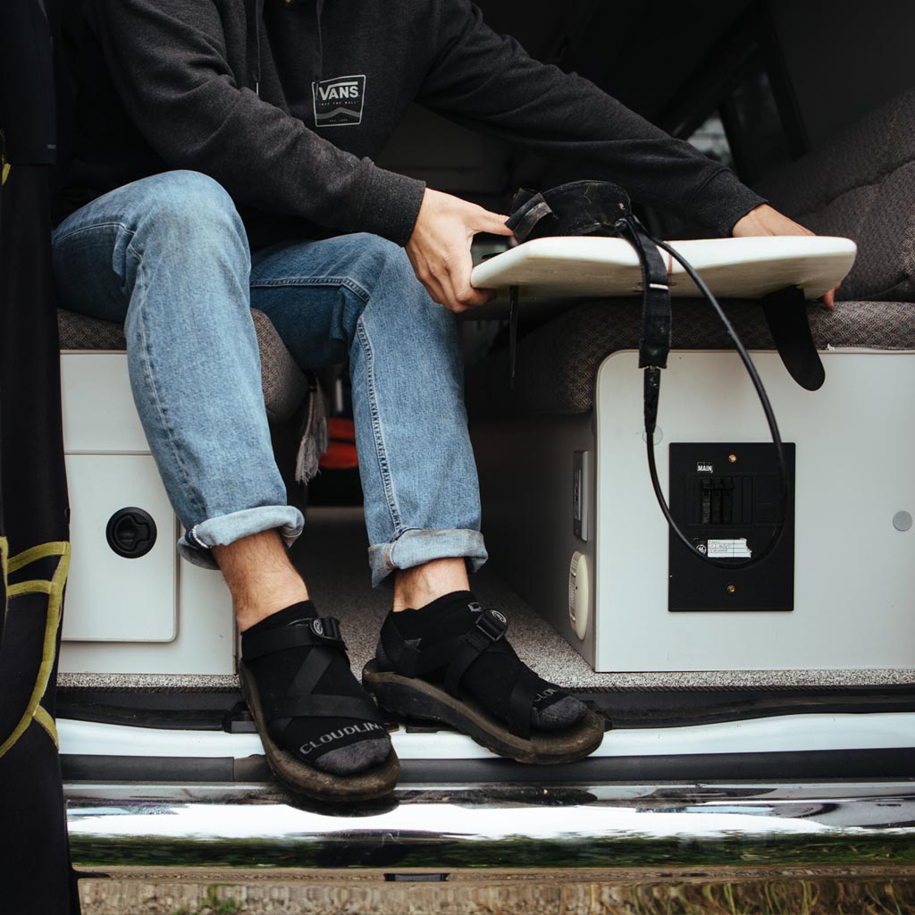 Man wearing Cloudline socks and sandals pulling surfboard out of van. 