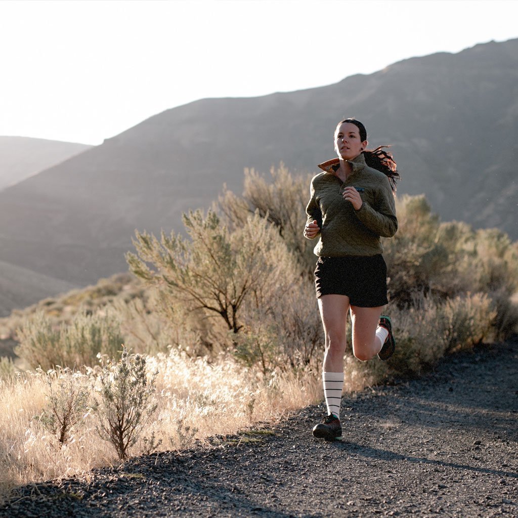Women wearing Cloudline socks running down gravel road surrounded by desert mountains. 
