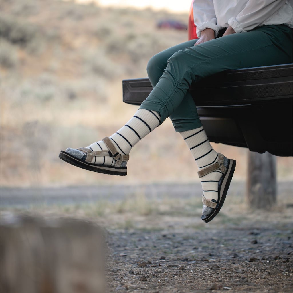 Women wearing Cloudling hiking socks with sandals dangling legs off the back of camper truck tailgate. 