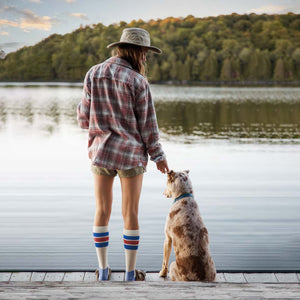 Women wearing Cloudline compression socks standing on dock with her dog watching the sunrise. 