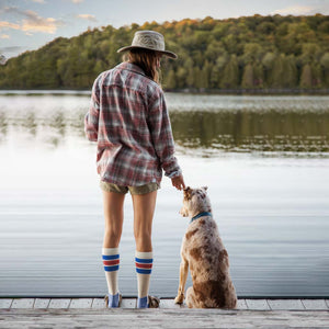 Women wearing Cloudline compression socks standing on dock with her dog watching the sunrise. 