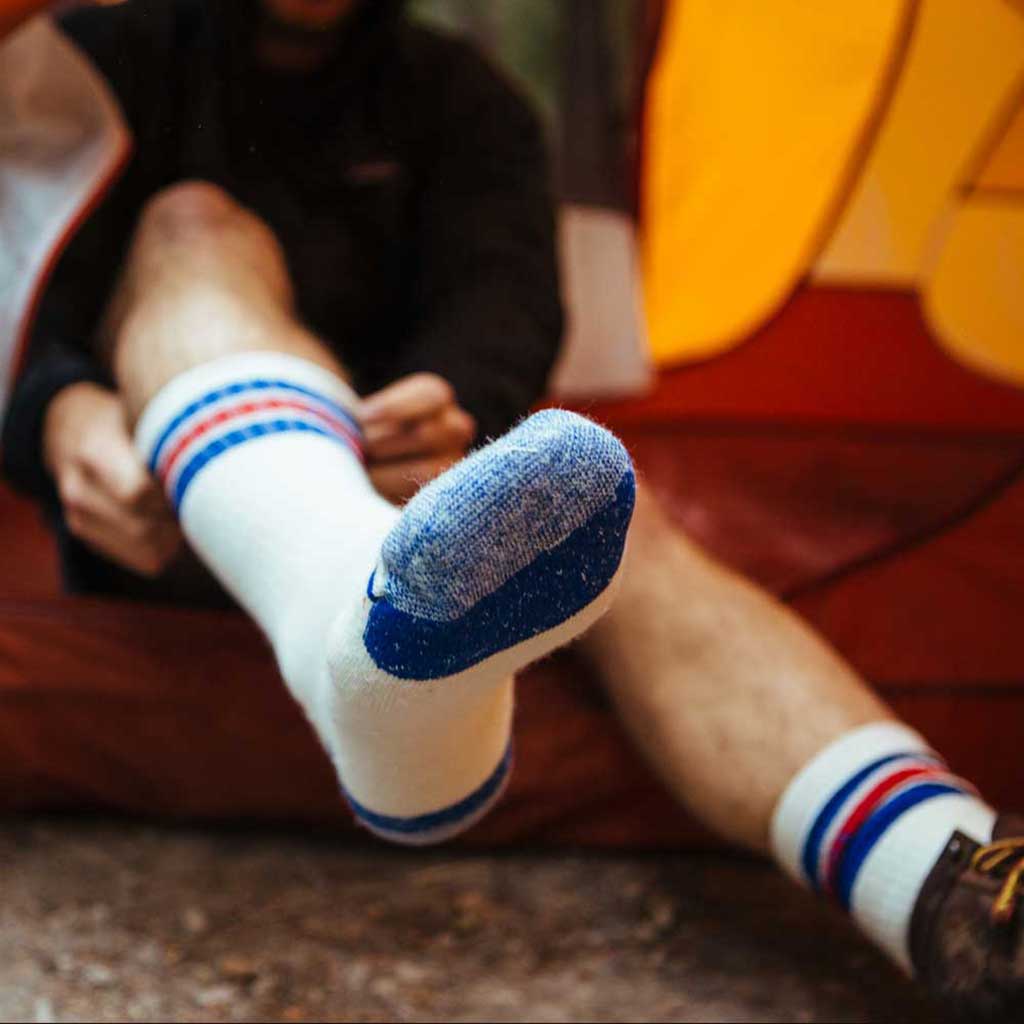 Man with feet sticking out of tent door pulling on Cloudline hiking socks. 