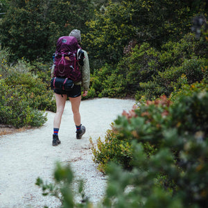 Backpacker wearing Cloudline hiking socks walking down trail into forest. 