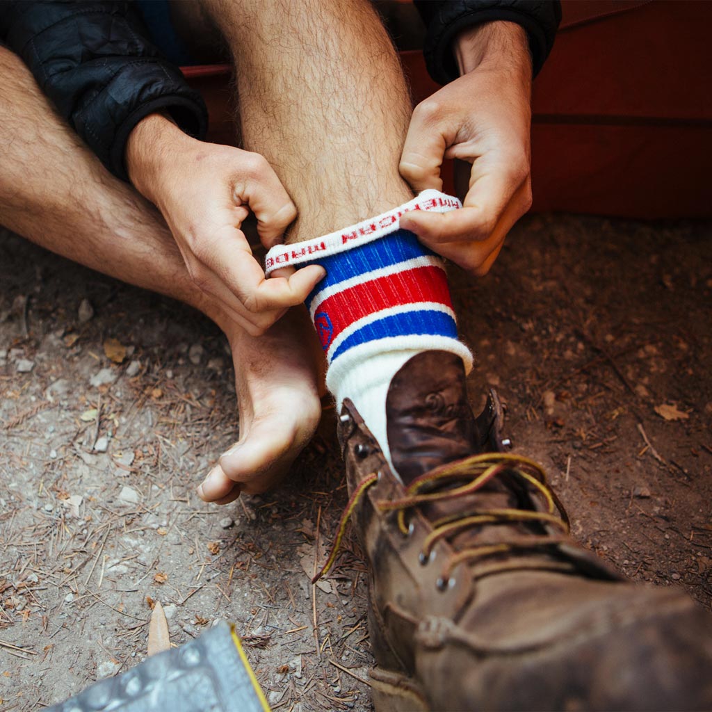 Man sitting in tent while pulling on Cloudline hiking socks.