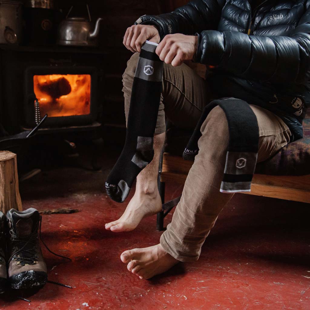 Man sitting on bed in cabin to pull on Cloudline snow socks.