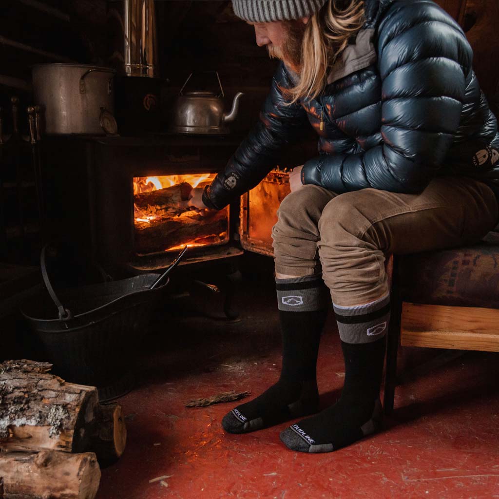 Man in cabin adding a log to wood stove while wearing Cloudline snow socks.