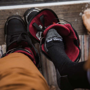 Snowboarder wearing Cloudline socks putting on snowboard boots.