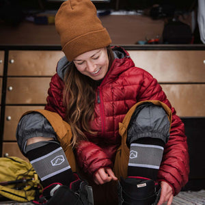 Women wearing Cloudline ski / snowboard socks sitting in camper van doorway putting on snow gear.
