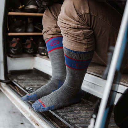 Man wearing Cloudline snowboard socks sitting in camper van with snowboard leaning next to him. 
