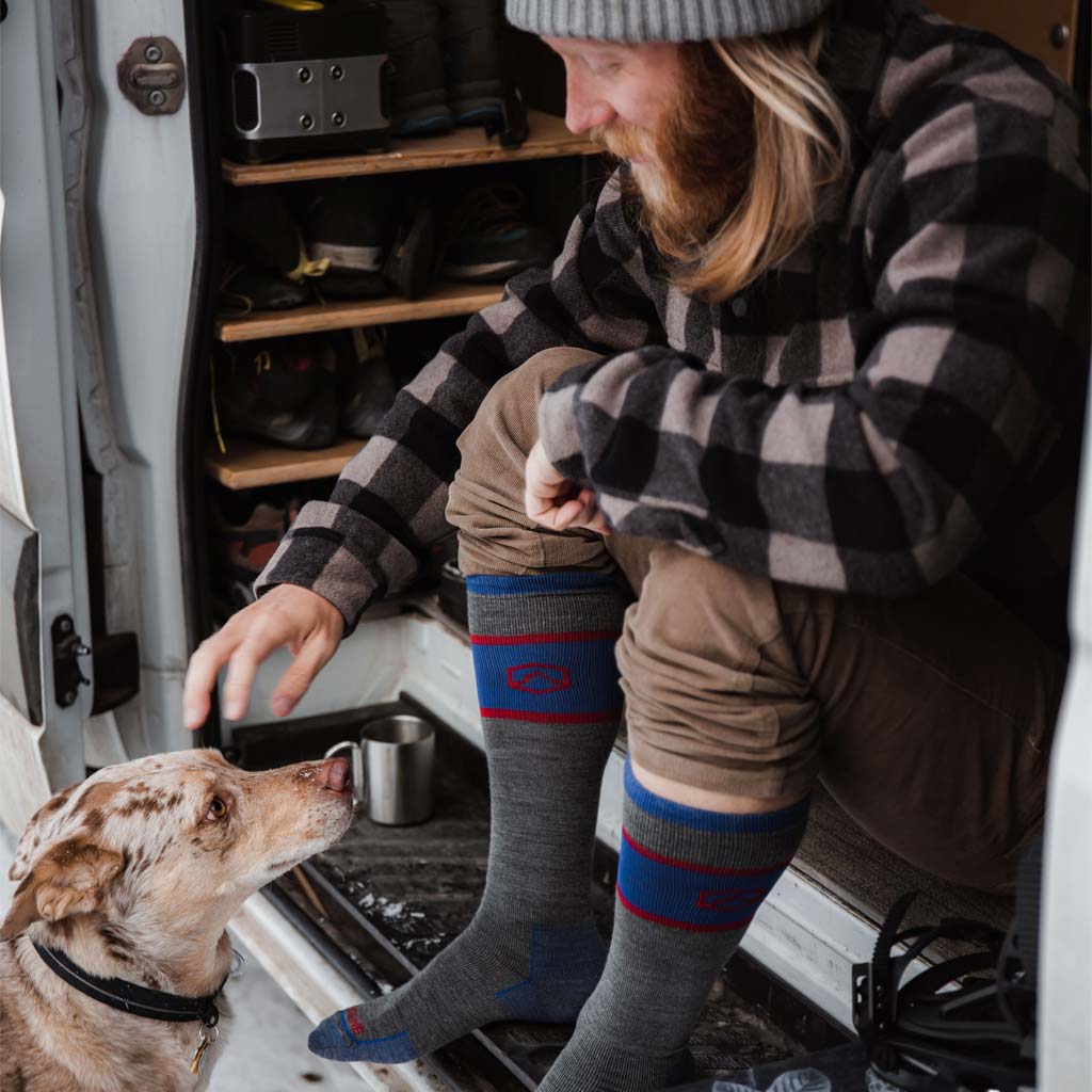 Man wearing Cloudline snowboard socks sitting in camper van petting dog.
