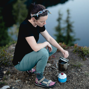 Backpacker wearing Cloudline merino tee crouched over backpacking stove boiling water. 