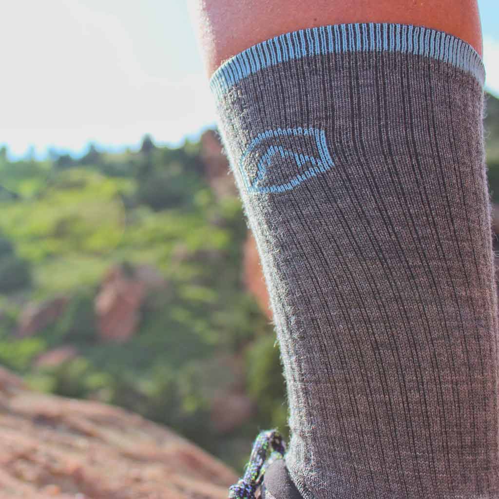 Close up of cloudline sock worn by women on trail with mountain in distance.