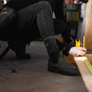 Women wearing Cloudline work socks crouched to measure board. 